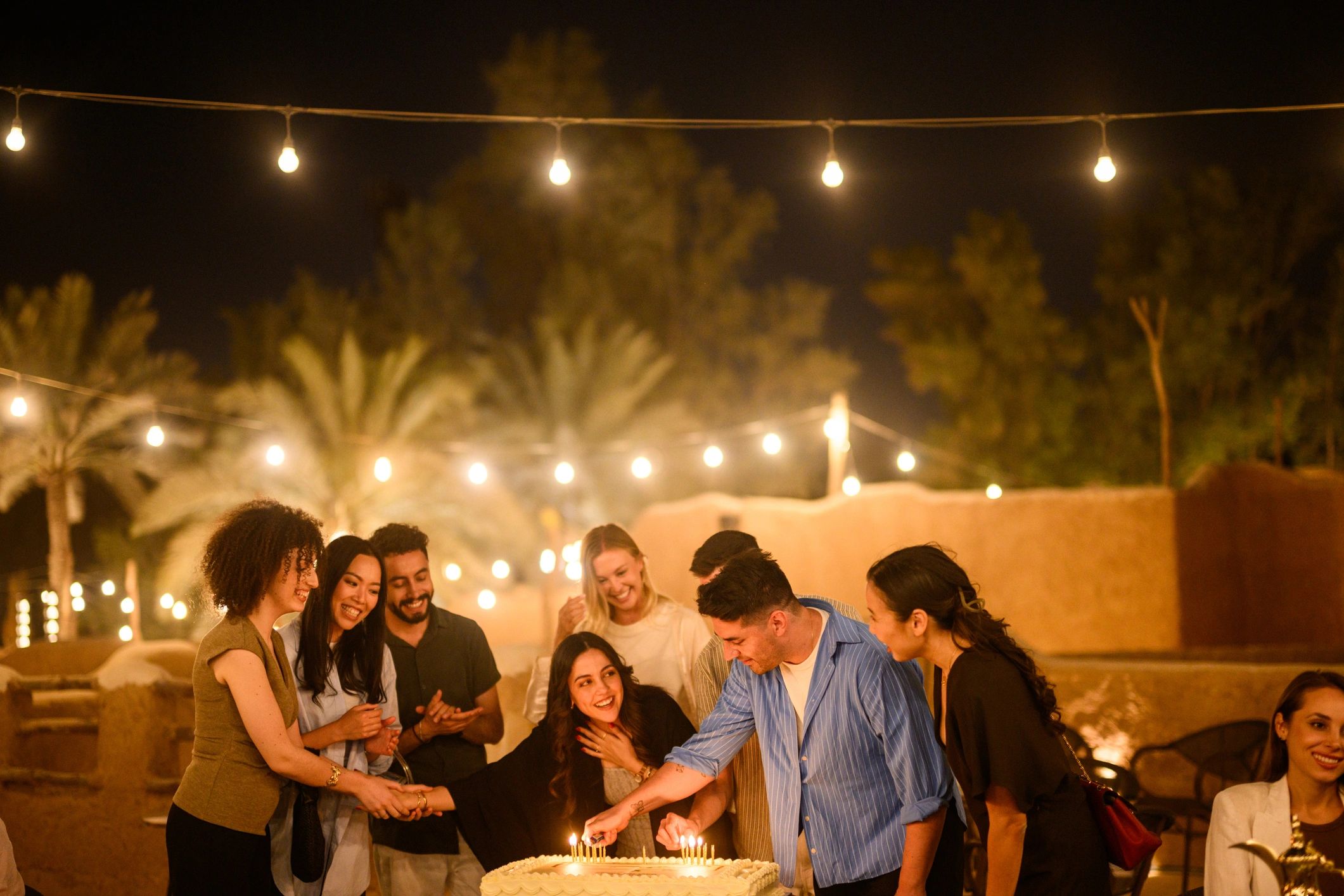 Friends gathered around a birthday cake under string lights